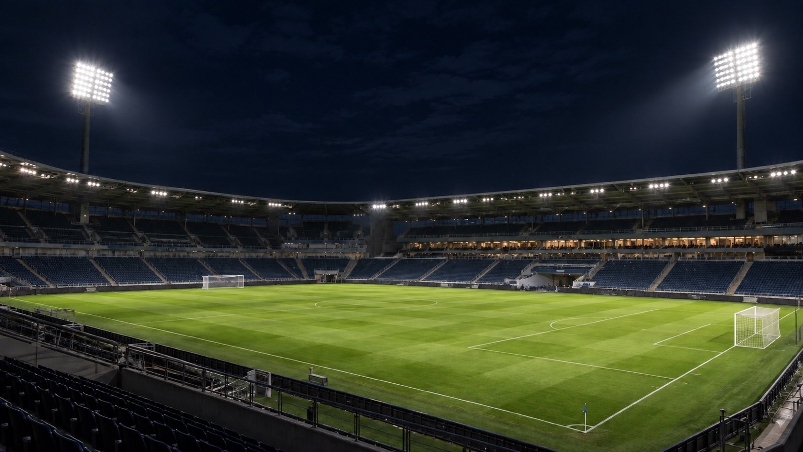 Futbolo stadionas vakare su stadiono prožektorių stiebais prie tribūnų ir žalia veja